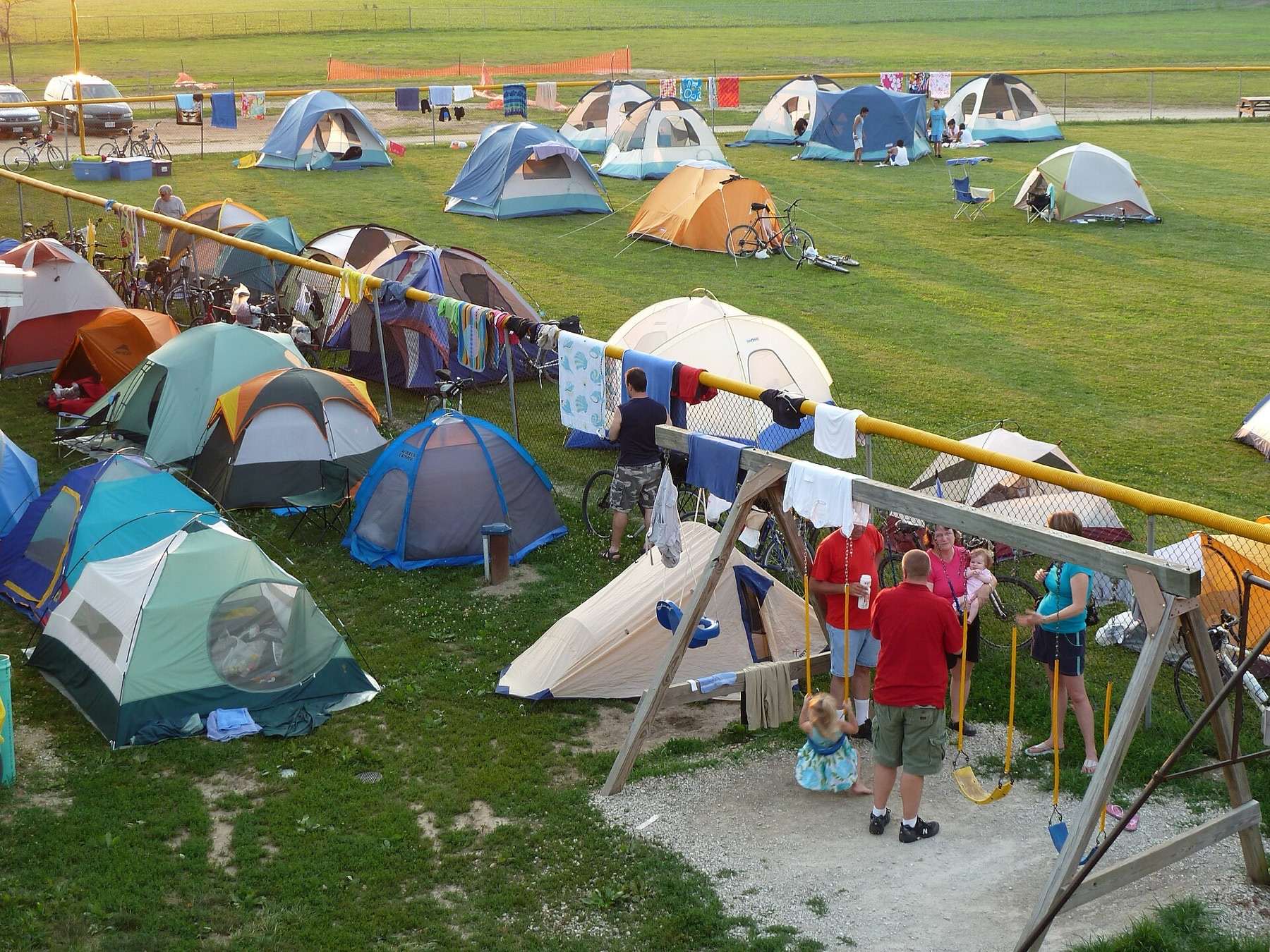 Several tents are pitched on a field in Katy Trail State Park in Missouri, with some children playing on the swings